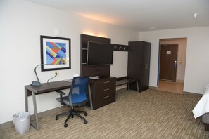 Ein Hotelzimmer mit Schreibtisch, Stuhl, Fernseher, Kleiderschrank und einem gerahmten Bild an der Wand.