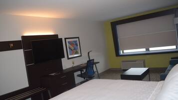 A hotel room with a bed, desk, chair, television, artwork, and a large window.