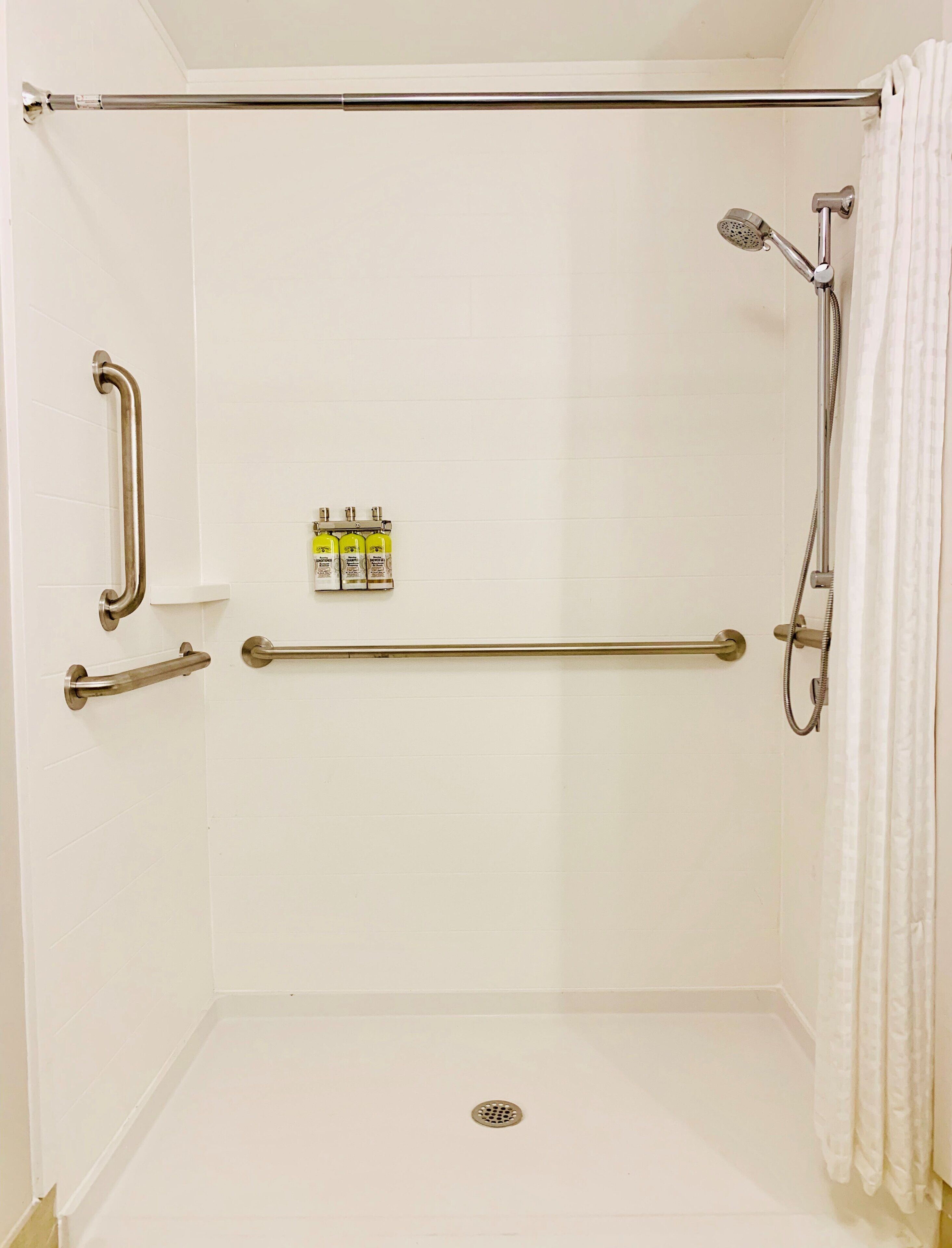 A shower area with a grab bar, a handheld showerhead, and a towel rack.