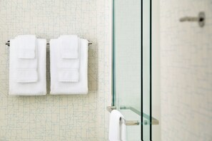 Ein Badezimmer mit Wandgestaltung im geometrischen Muster, einer Duschkabine aus Glas und zwei weißen Handtüchern an einem Handtuchhalter.
