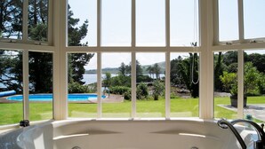 A large windowed room with a view of a swimming pool and a lake. - Luxury House on Seafront, with Pool, Sauna, Jacuzzi and Woodlands (castletownbere)