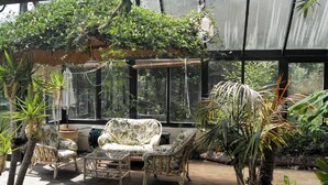 A conservatory with wicker furniture, large windows, and tropical plants. - Luxury House on Seafront, with Pool, Sauna, Jacuzzi and Woodlands (castletownbere)