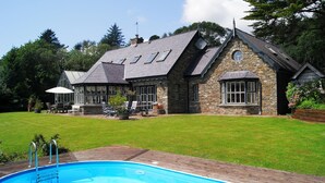 A house with a stone exterior, a swimming pool, and a patio area with outdoor furniture. - Luxury House on Seafront, with Pool, Sauna, Jacuzzi and Woodlands (castletownbere)