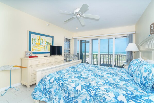 Une chambre avec un grand lit, un ventilateur de plafond, une télévision, un tableau et un balcon avec vue.