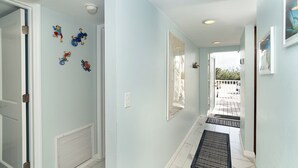Un couloir aux murs bleu clair, avec une grille d’aération, un miroir et une porte.