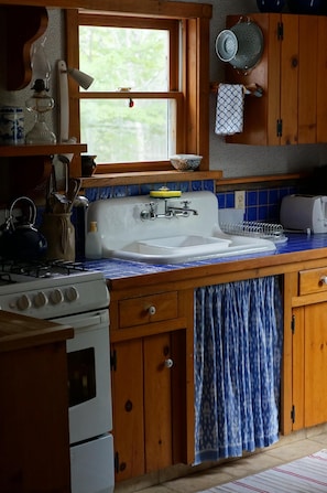 Kitchen features a stove, sink, and wooden cabinets, with a window and pot rack.