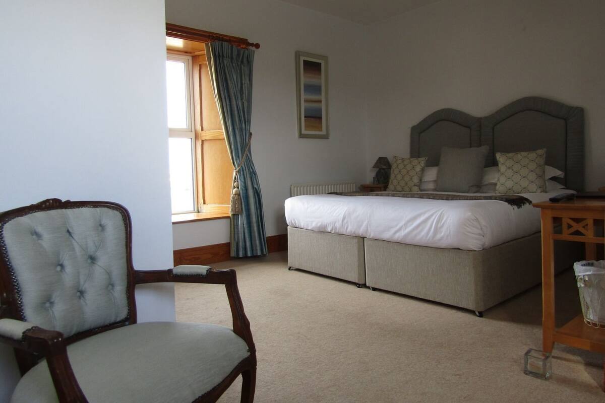 A bedroom with a bed, a chair, a bedside table, and a window with curtains.