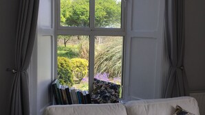 Una habitación con un sofá blanco, una ventana con cortinas y vistas a un jardín.