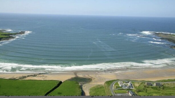 Vista aérea de una zona costera con playa, carretera y algunos edificios.