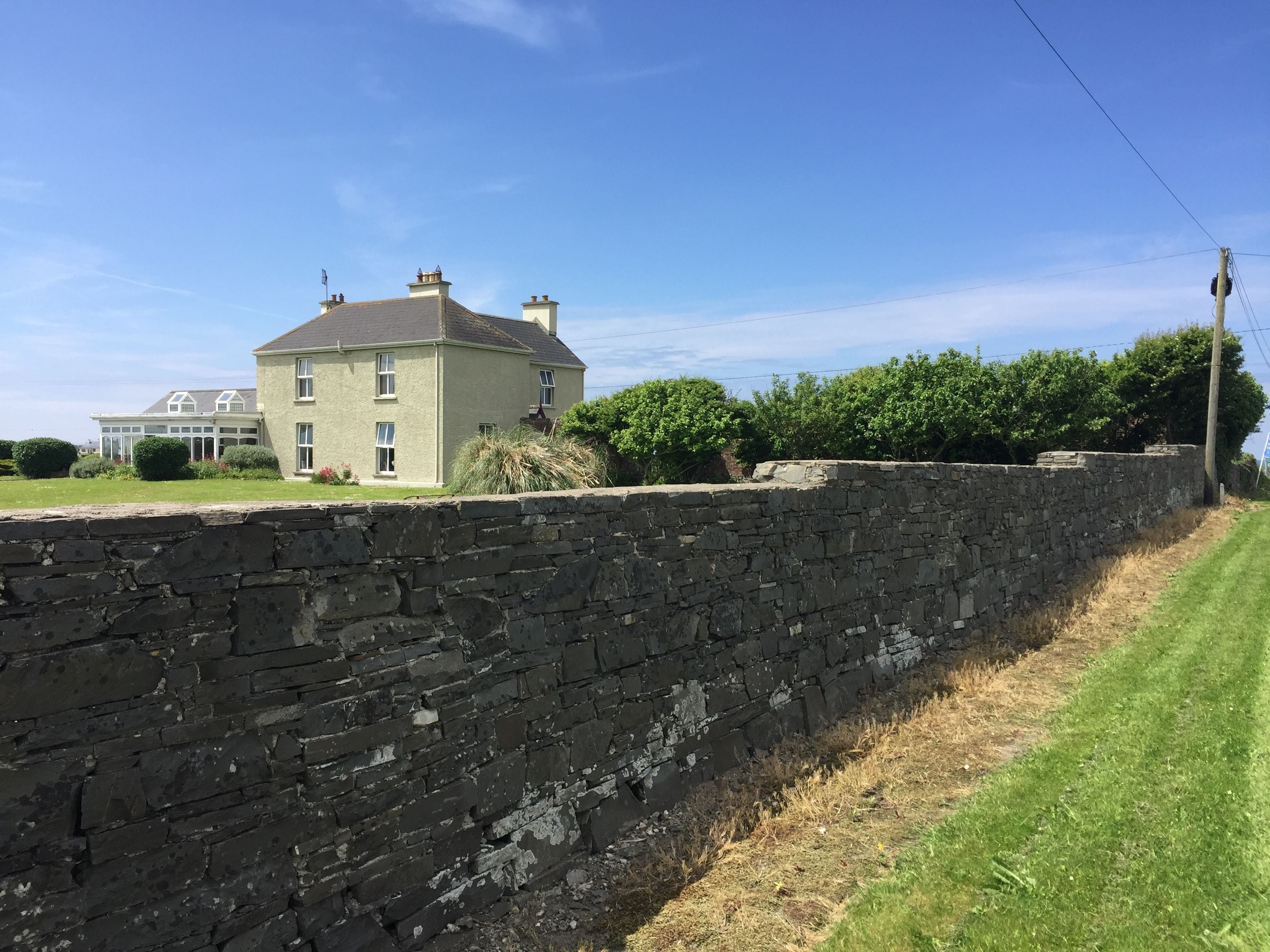 Un mur de pierre, une zone herbeuse et une grande maison avec de nombreuses cheminées.