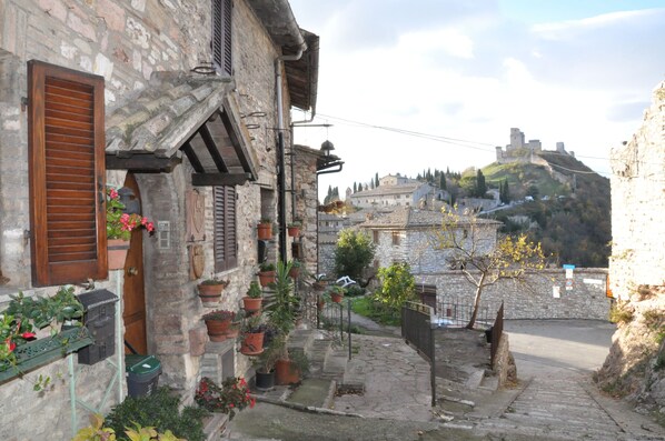 A narrow cobblestone street with stone buildings, a bell tower, and a castle on a hill in the background.