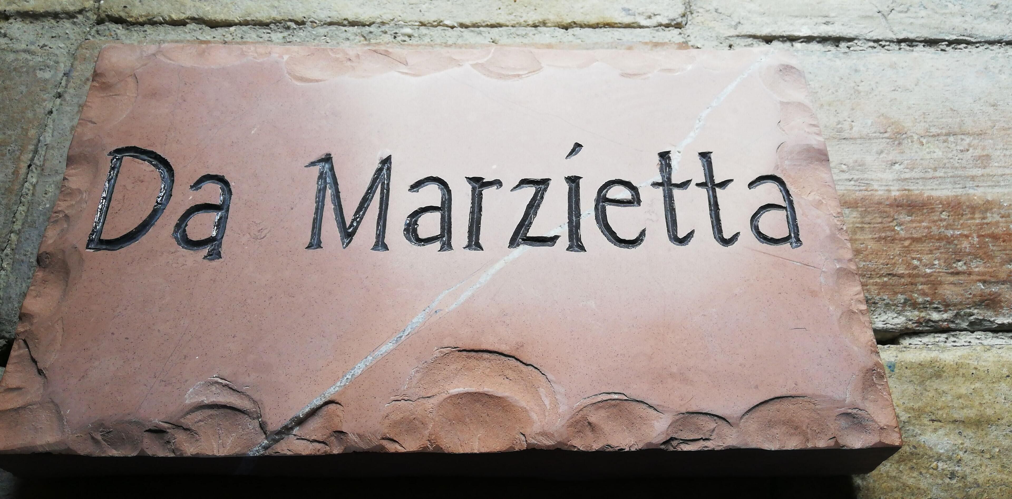 A terracotta plaque with the inscription "Da Marzietta" on a stone wall.
