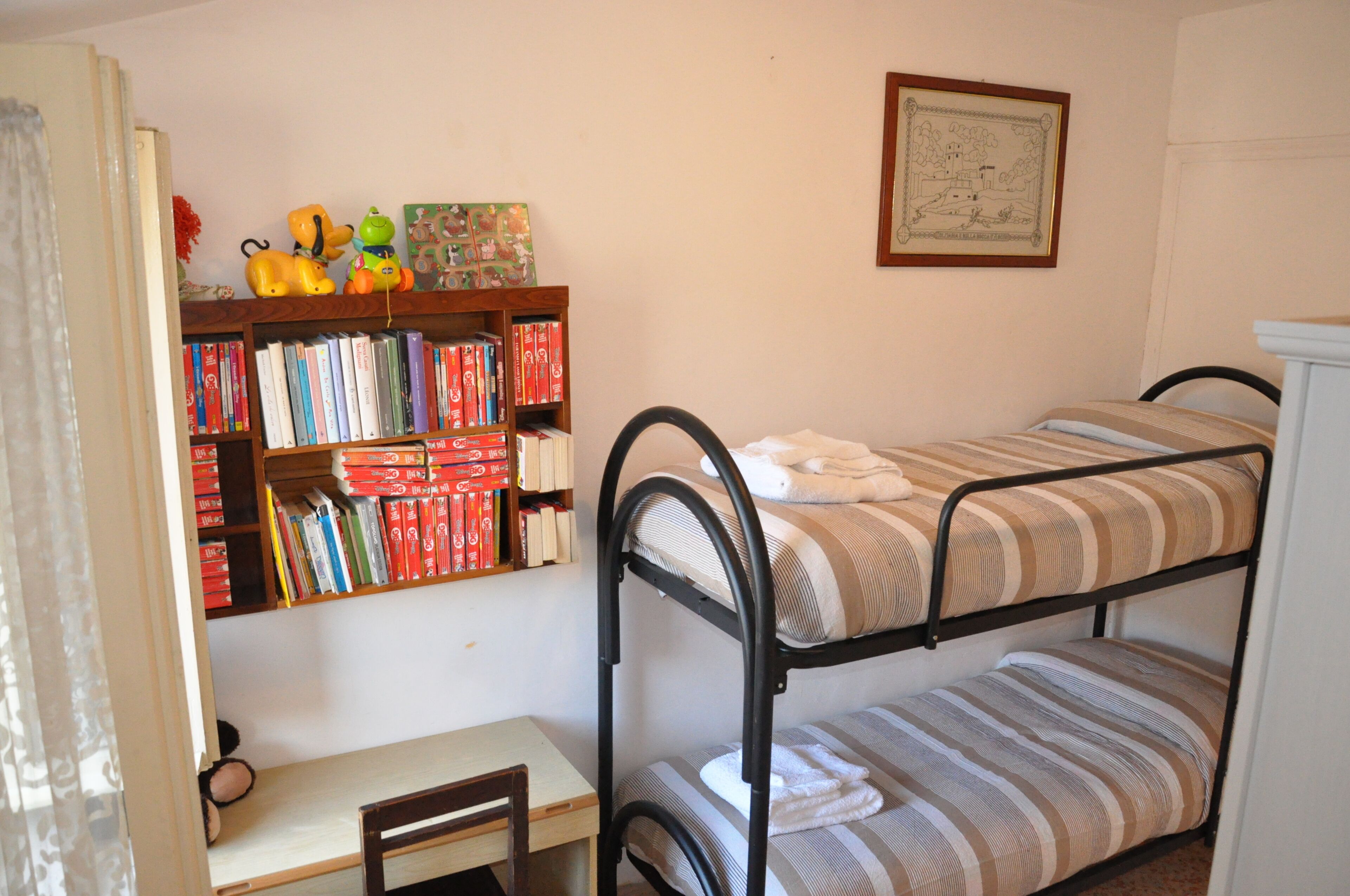 Un lit superposé avec une literie à rayures, une bibliothèque en bois remplie de livres et de jouets, et un tableau encadré accroché au mur.