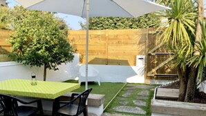 Eine Terrasse mit Tisch und Stühlen, eine Holzterrasse, ein weißer Zaun und ein kleiner Garten mit einer Palme.