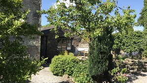 A stone building with a small garden area, including a tree and various shrubs. - Traditional Lakeland Hideaway Cottage for two, close to the Lakes and Dales (KENDAL)