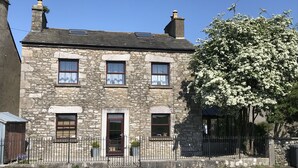A stone building with a traditional design, featuring a central entrance, multiple windows, and a small garden area. - Traditional Lakeland Hideaway Cottage for two, close to the Lakes and Dales (KENDAL)