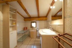Ein kleines Badezimmer mit Holzbalkendecke, Waschbecken und Spiegel.