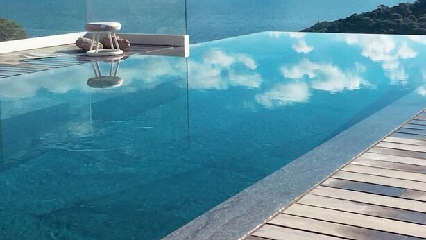 A clear blue infinity pool with a wooden deck, overlooking a mountainous landscape and the sea. - VILLA LUXE SA TUNA, heated mirror pool VERY BEAUTIFUL SEA VIEW (Begur)