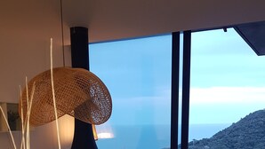 A modern living room with a large window overlooking a coastal landscape, a black floor lamp, and a cozy seating area. - VILLA LUXE SA TUNA, heated mirror pool VERY BEAUTIFUL SEA VIEW (Begur)