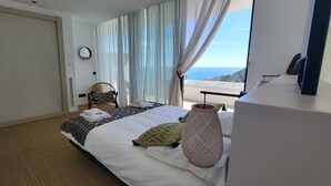 A hotel room with a bed, a chair, a large window with curtains, and a view of the sea. - VILLA LUXE SA TUNA, heated mirror pool VERY BEAUTIFUL SEA VIEW (Begur)