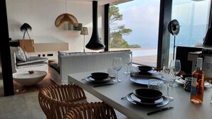 A dining area with a table set for two, a view of the sea, and a modern interior design. - VILLA LUXE SA TUNA, heated mirror pool VERY BEAUTIFUL SEA VIEW (Begur)