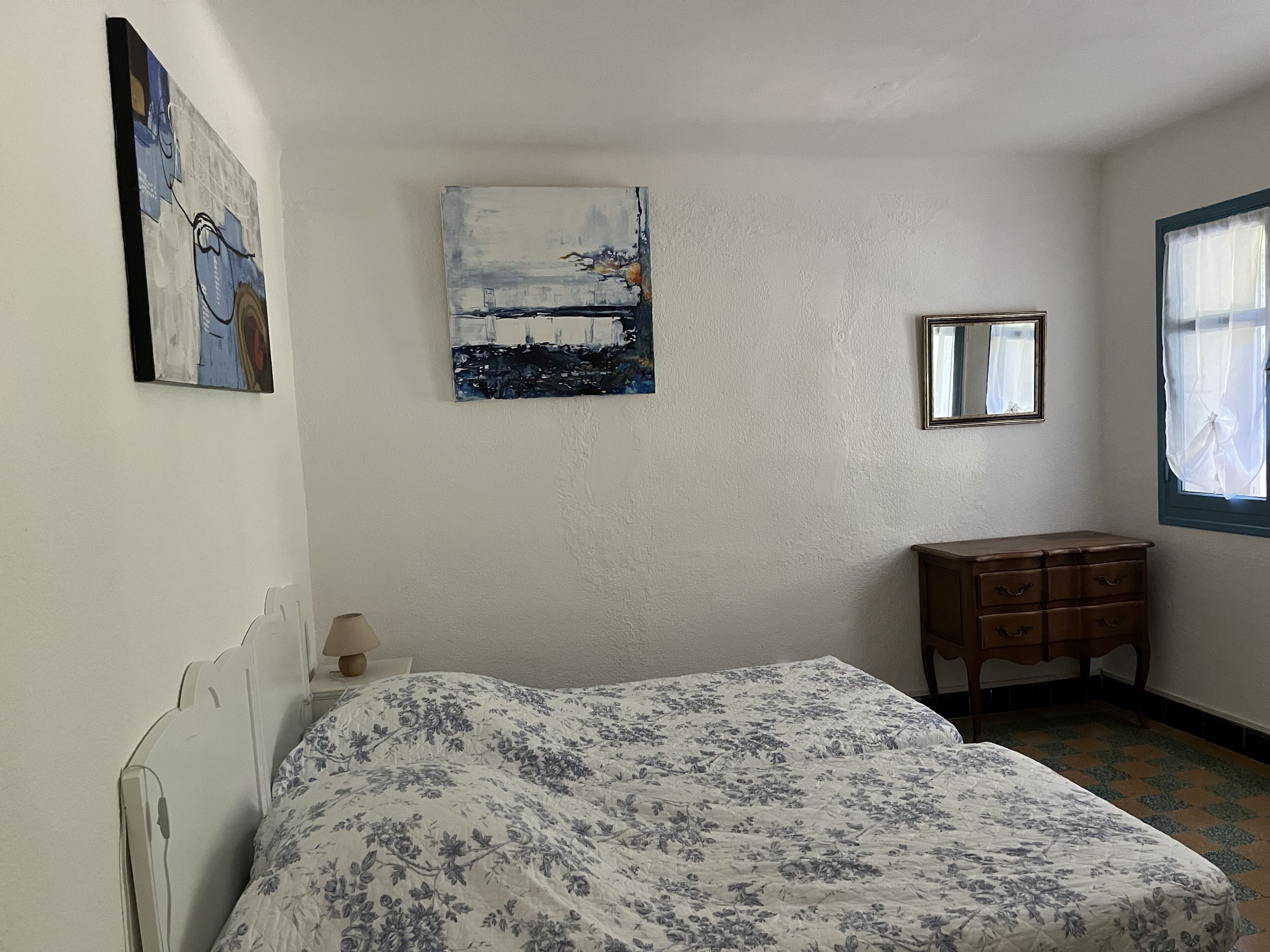 A bedroom with a bed, a dresser, a painting, and a window.