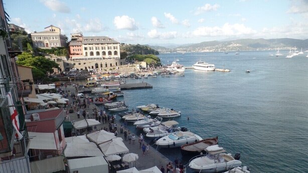 A coastal marina with boats docked and people walking along the pier.
