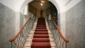 A marble staircase with red carpet runners, metal railings, and a wooden handrail.