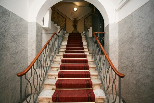 A marble staircase with red carpet runners, metal railings, and a wooden handrail.