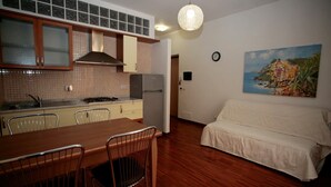 A compact kitchen with a dining area, a sofa, and a painting on the wall.