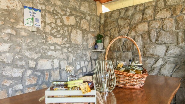 A rustic stone wall with a wooden table, a wicker basket with bottles, a glass vase, and a QR code sign. - Holiday house Roža * large garden, sun terrace, BBQ, free WiFi (Labin)