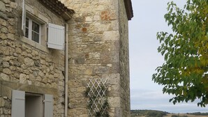 A stone building with a tiled roof, a white table with chairs, a barbecue grill, and a view of the countryside. - 18th century Gersoise house, secluded, swimming pool, wooded grounds (La Romieu)