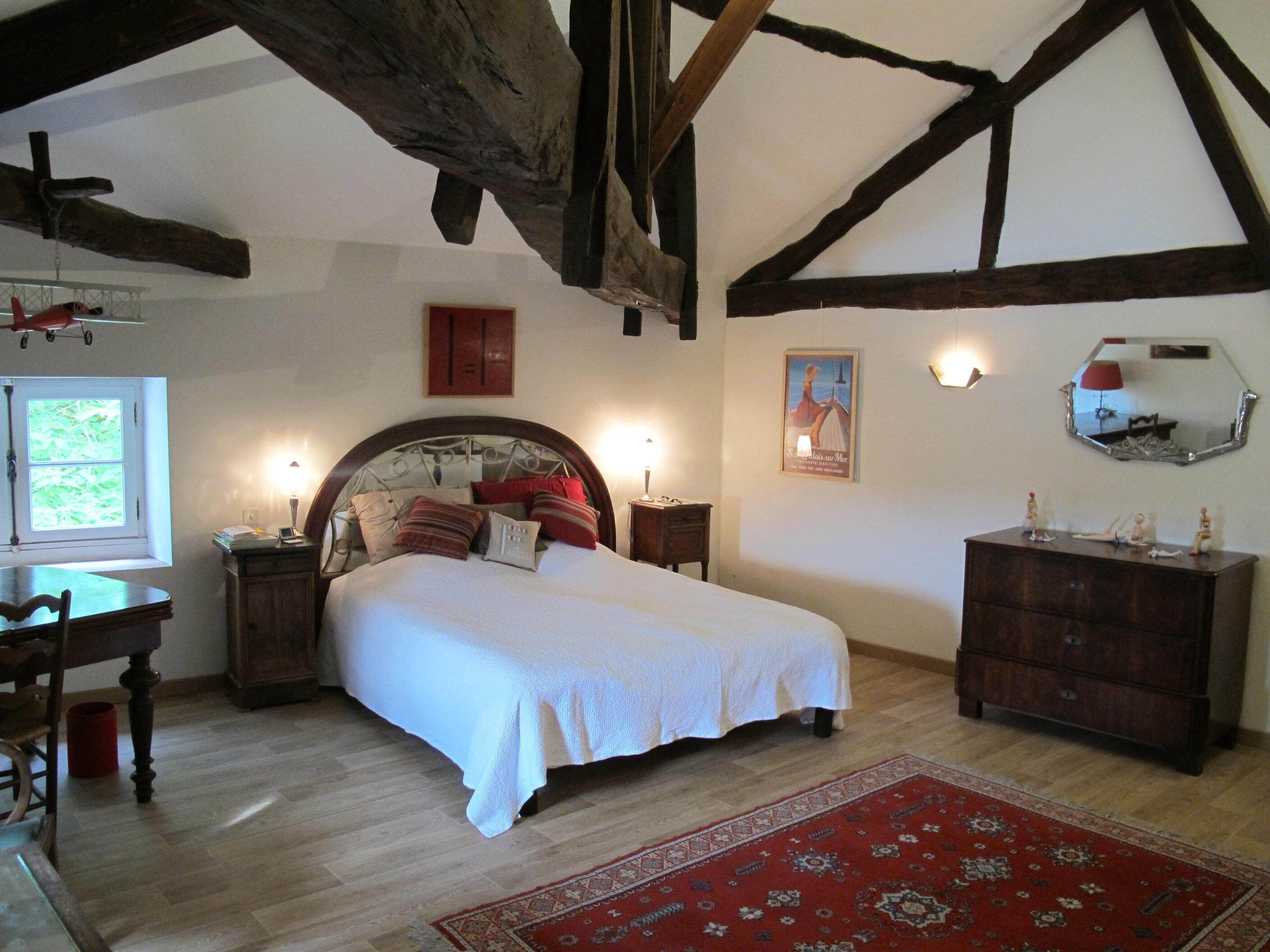 Une chambre avec un plafond en bois, un lit avec une literie blanche, un tapis rouge et une commode.