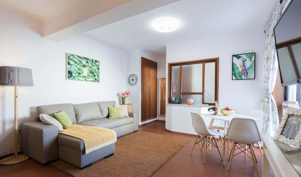 A living room with a sofa, a dining table with chairs, a lamp, and artwork on the walls.