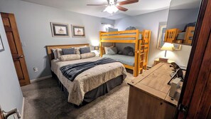 A bedroom with a bunk bed, a desk, a mirror, and two framed pictures on the wall.