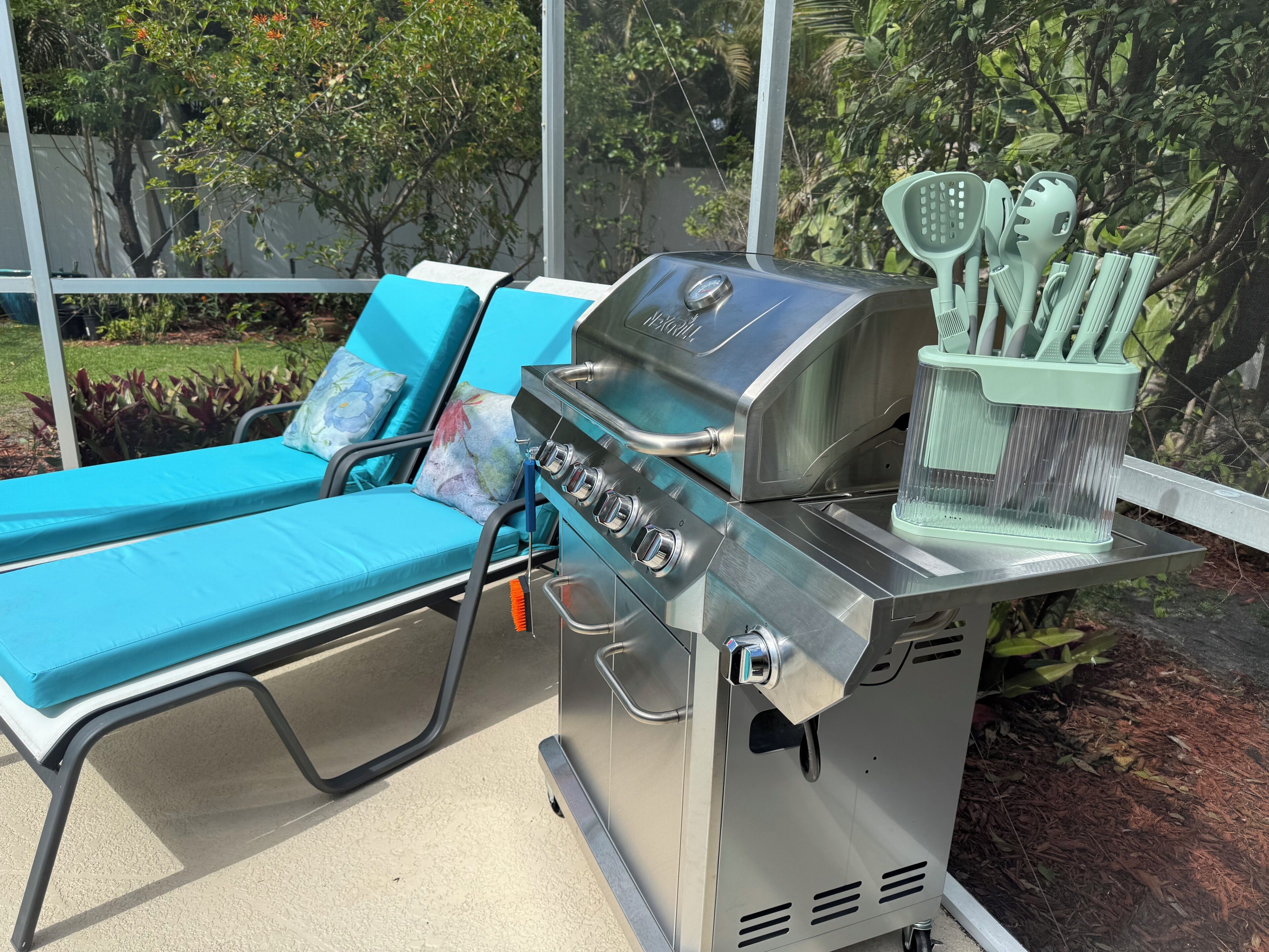 Un espace extérieur aménagé avec un barbecue, des chaises longues et une vue sur la verdure.