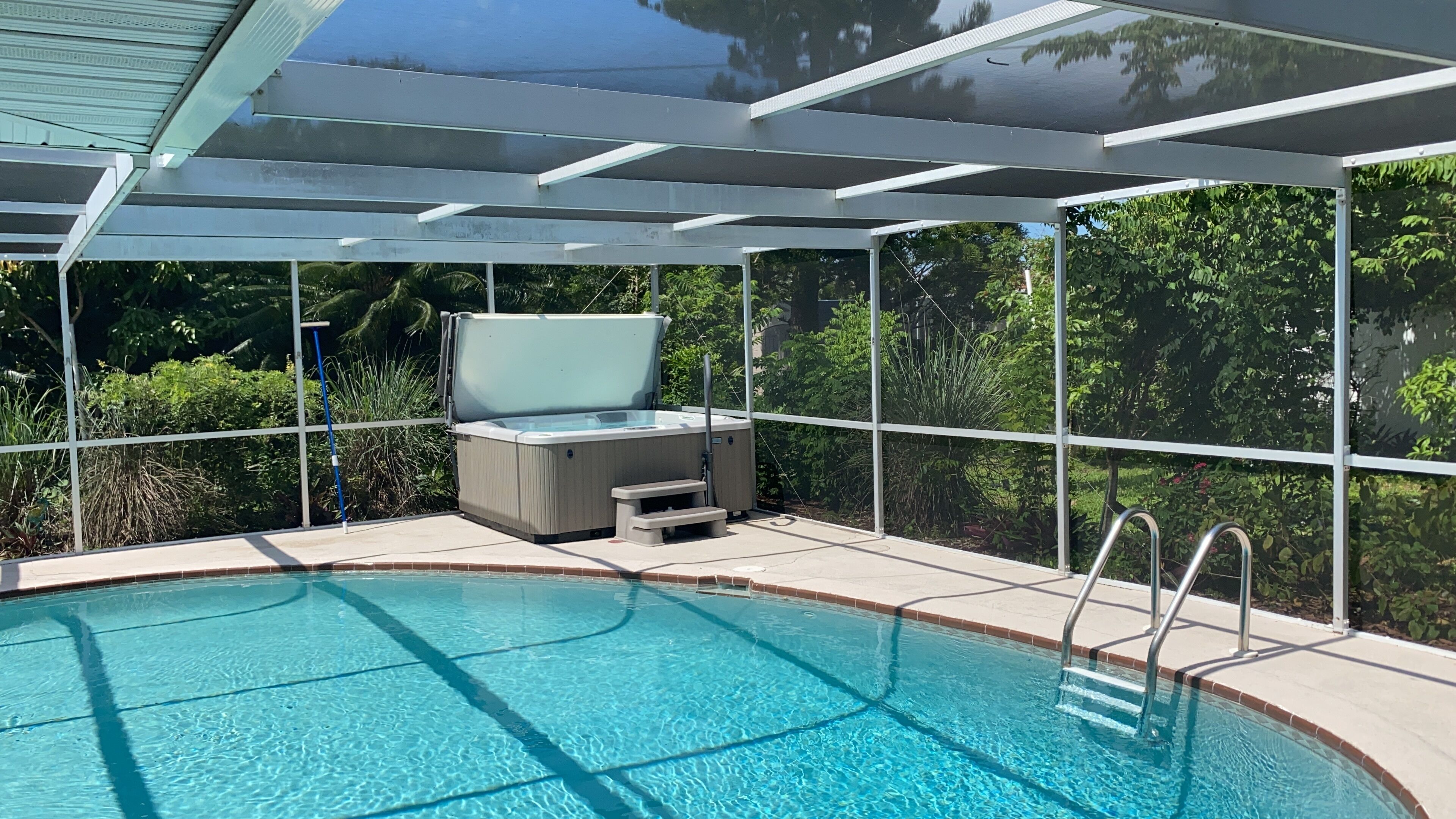 Una piscina con un jacuzzi, rodeada por un cerramiento de vidrio y una barandilla de metal.