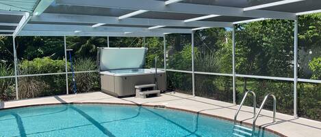 Una piscina con un jacuzzi, rodeada por un cerramiento de vidrio y una barandilla de metal.