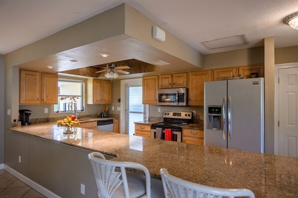 A spacious kitchen with granite countertops, wooden cabinets, stainless steel appliances, and a central island with seating.