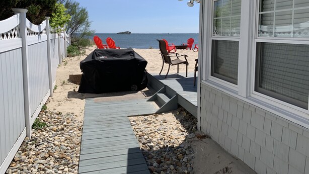 Una terraza con una parrilla, sillas rojas y vistas a la playa y el océano.