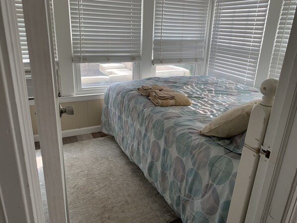 A bedroom with a bed, a window with blinds, a door, and a carpeted floor.