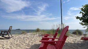 Una playa con dos sillas Adirondack rojas y una silla marrón.