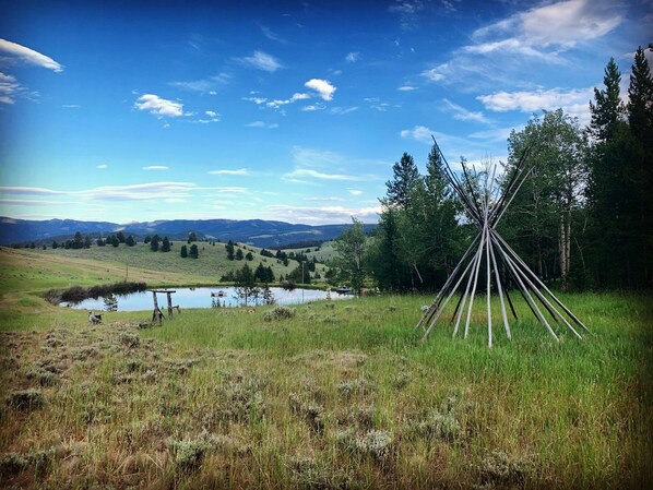 A serene landscape with a teepee, a small pond, and distant mountains under a clear sky.