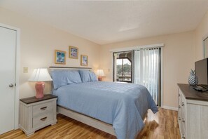 A bedroom with a bed, bedside tables, a lamp, a window with curtains, and a television on a cabinet.