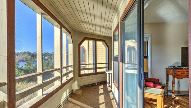 A spacious balcony with large windows offering a view of a lake and trees.