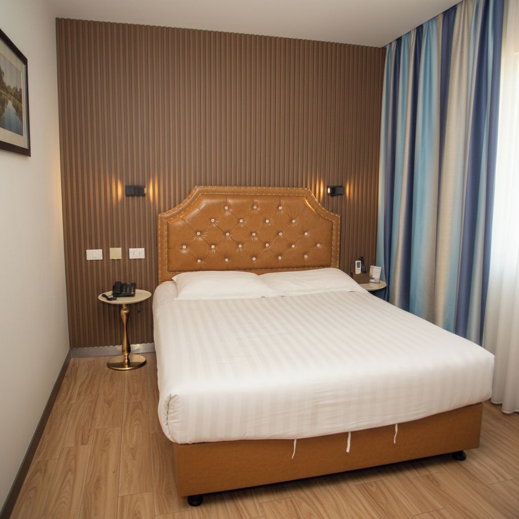 A hotel room with a large bed, a bedside table with a phone, and a wall-mounted light.