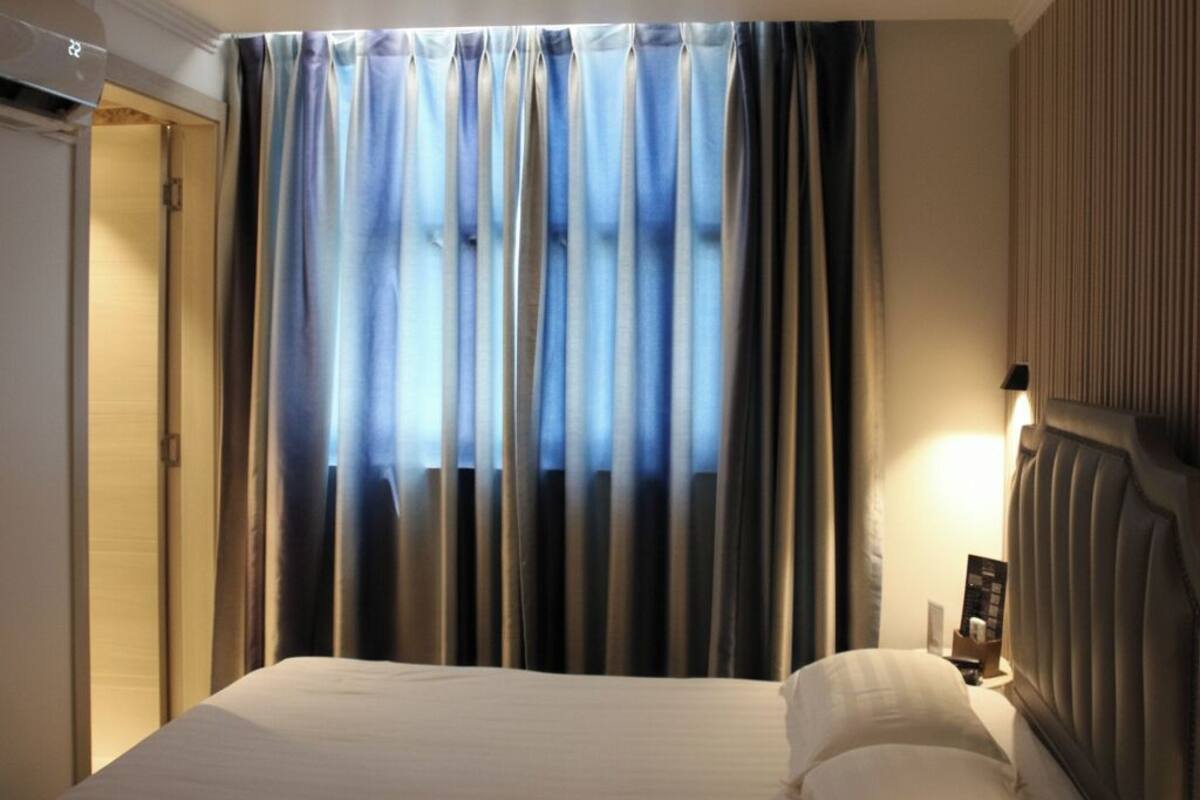 Quarto de hotel com cama, cortinas, mesa de cabeceira e luminária na parede.