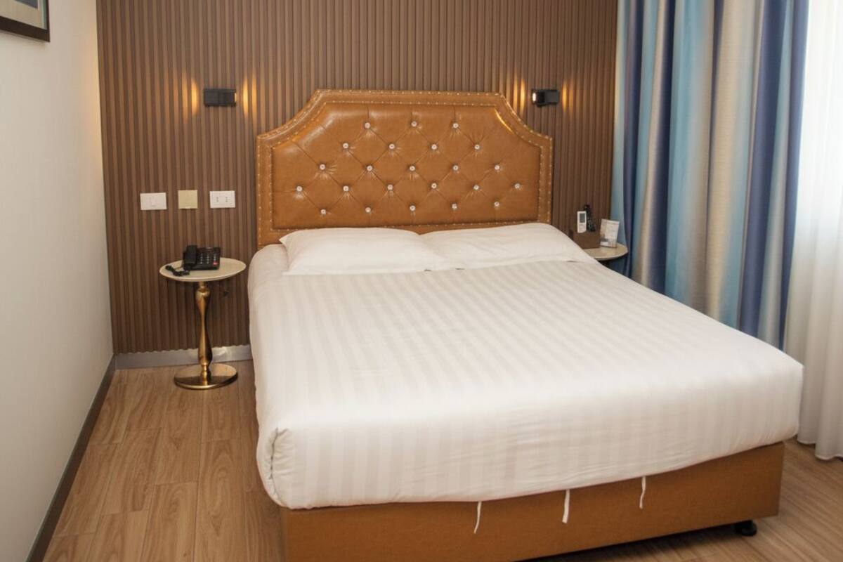 Quarto de hotel com cama grande, mesa de cabeceira com telefone e luminária na parede.