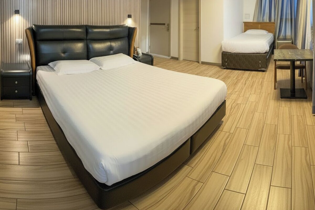 A hotel room with a large bed, a desk, a chair, an air conditioning unit, and a door leading to another room.