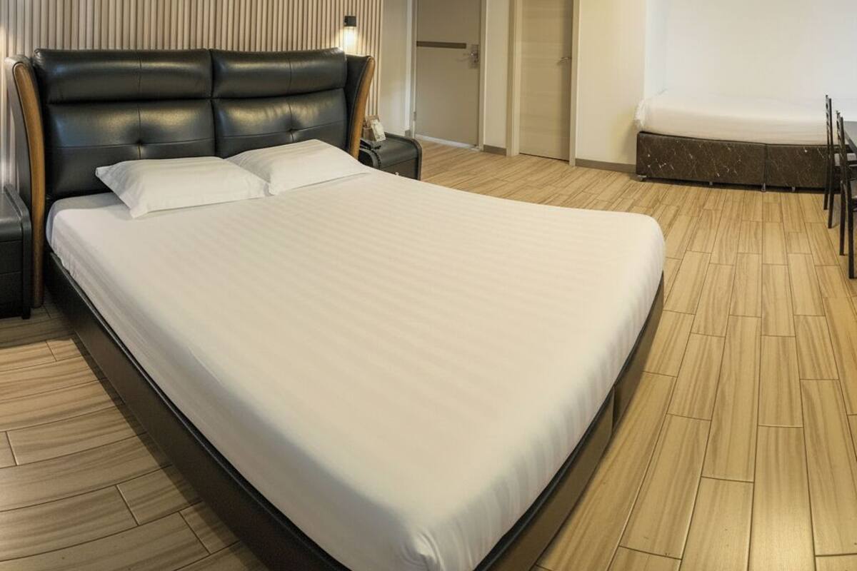 Quarto de hotel com uma cama grande, uma escrivaninha, uma cadeira, um ar condicionado e uma porta que dá para outro cômodo.